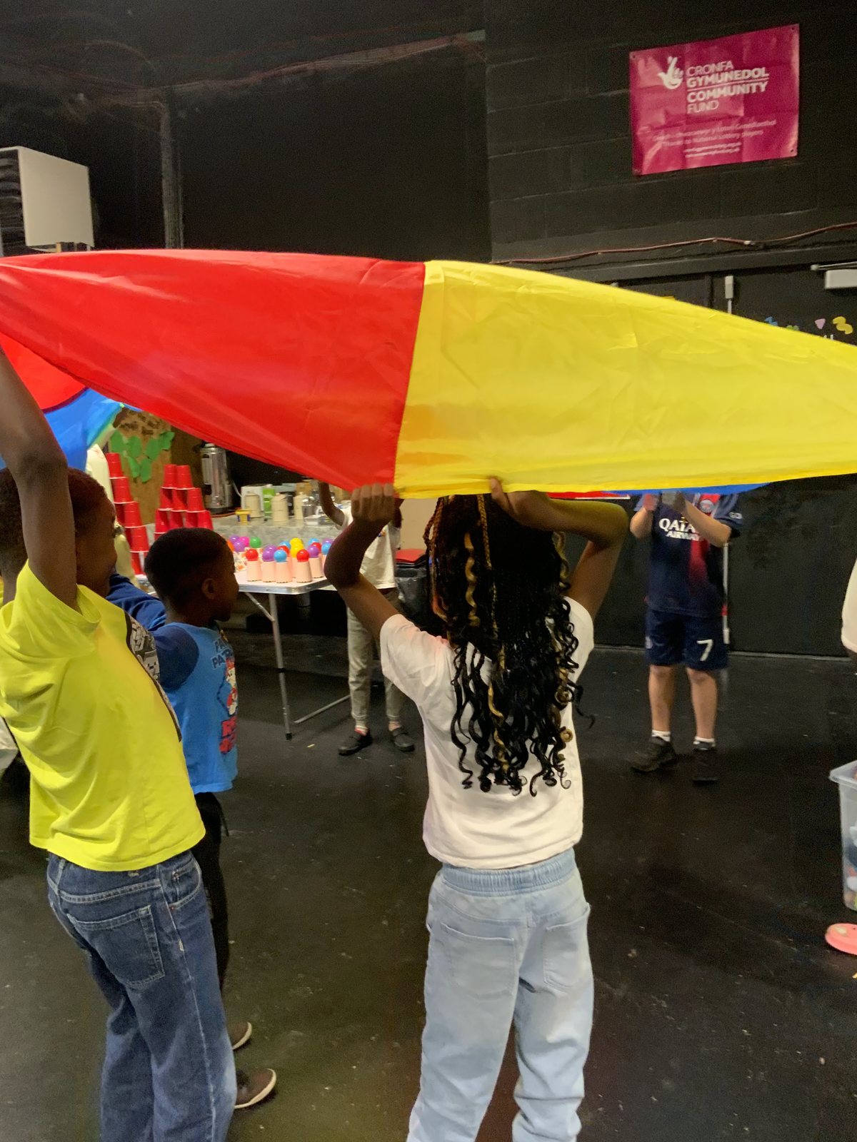 Children standing in a circle holding the edge of a red and yellow parachute above their heads.