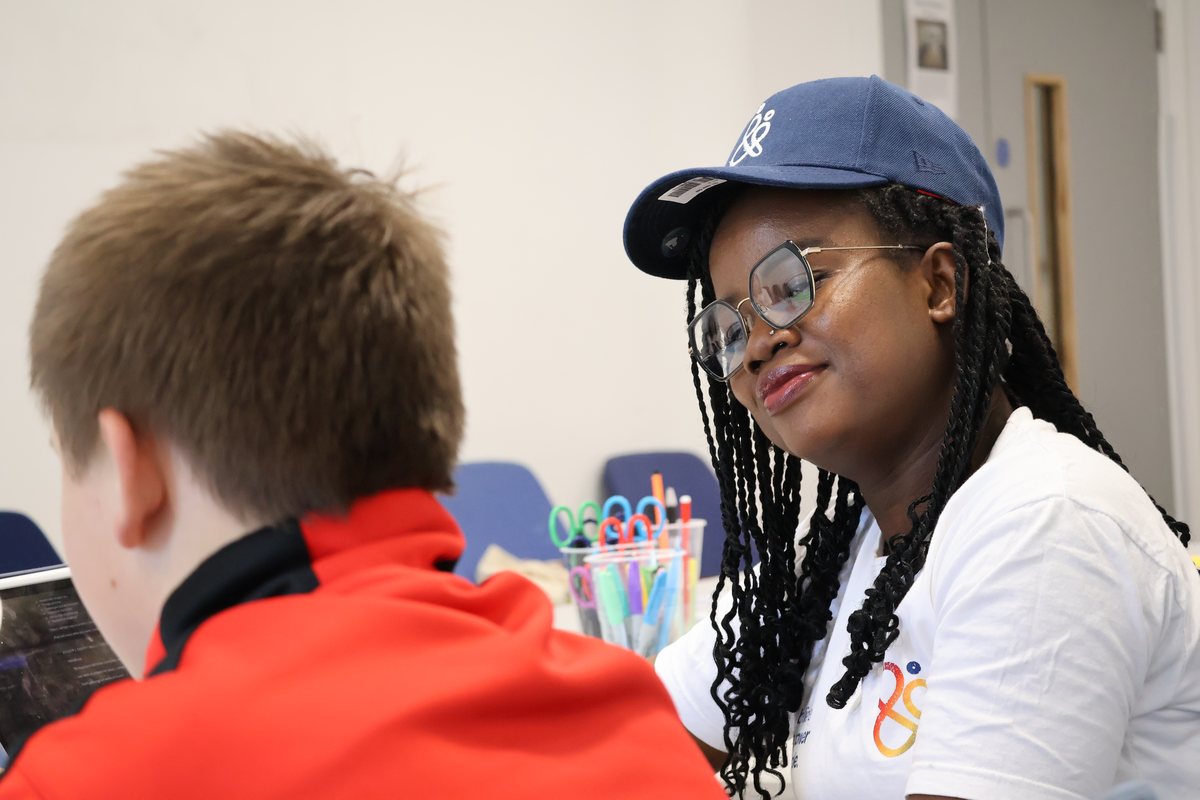 A facilitator in a Benzone T-shirt leaning in to talk with a young person across a table.