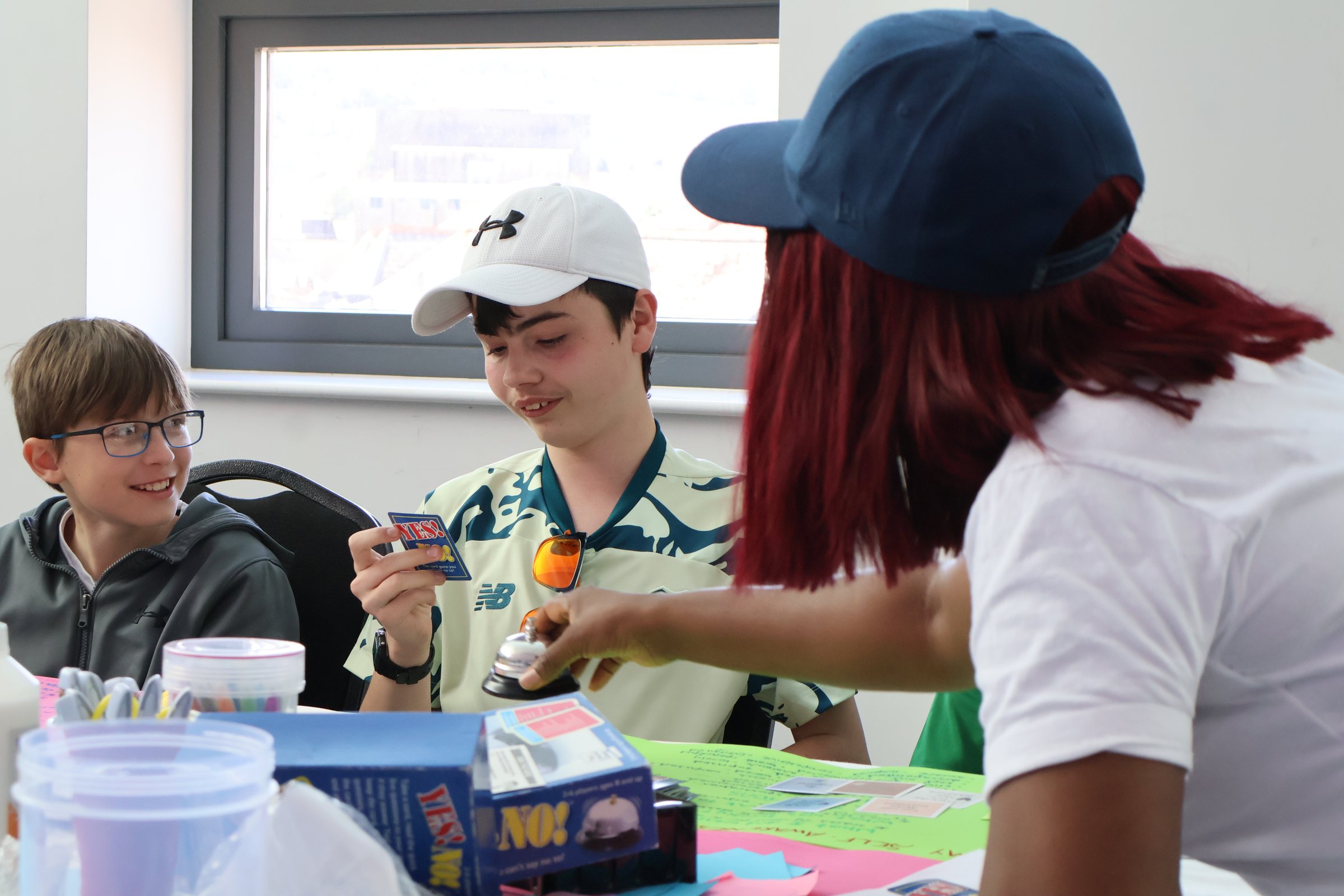 Young people around a craft table, one holding up what he has made while the others look on.
