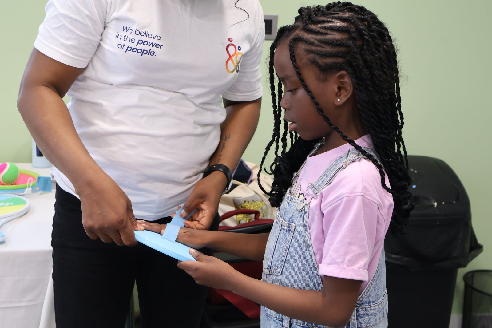 A facilitator standing beside a young girl, helping her with the piece she is making.