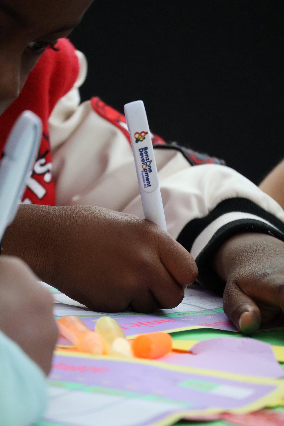 close shot of a young person writing on paper with a branded Benzone pen