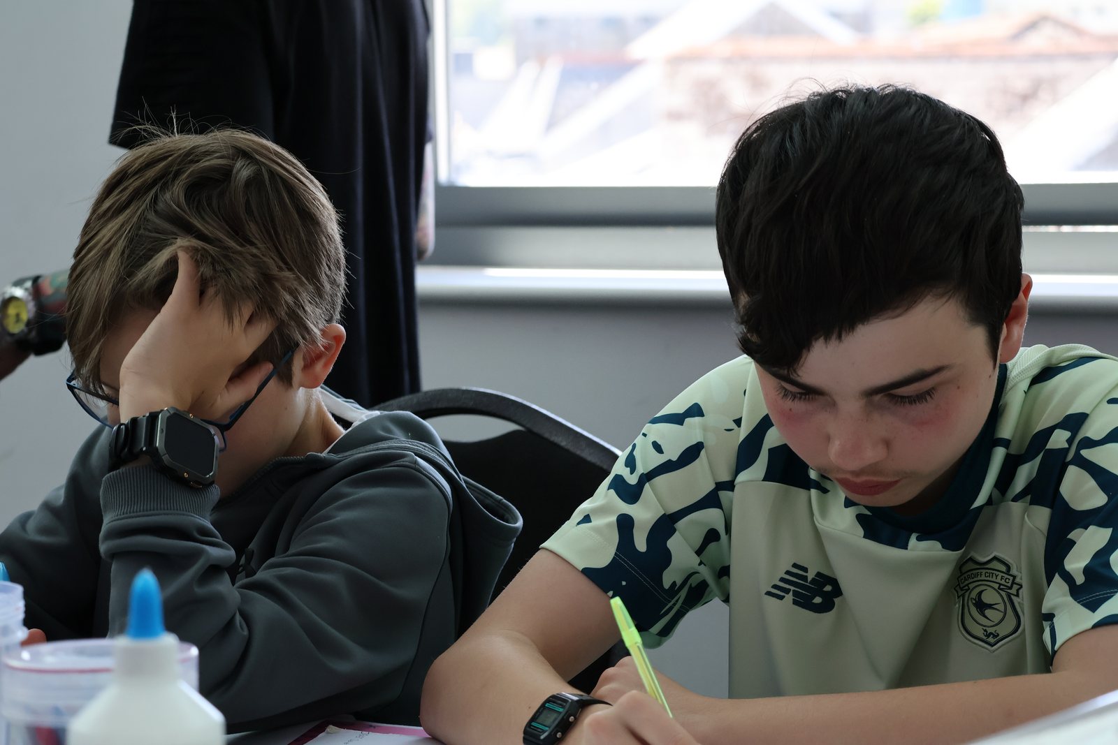 Two boys working side by side at a table, one writing with a highlighter, both absorbed in the task.