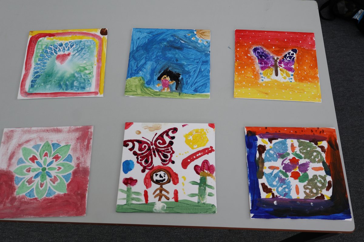 Six finished paintings laid out on a table: butterflies, flowers and abstract patterns in bright colours.