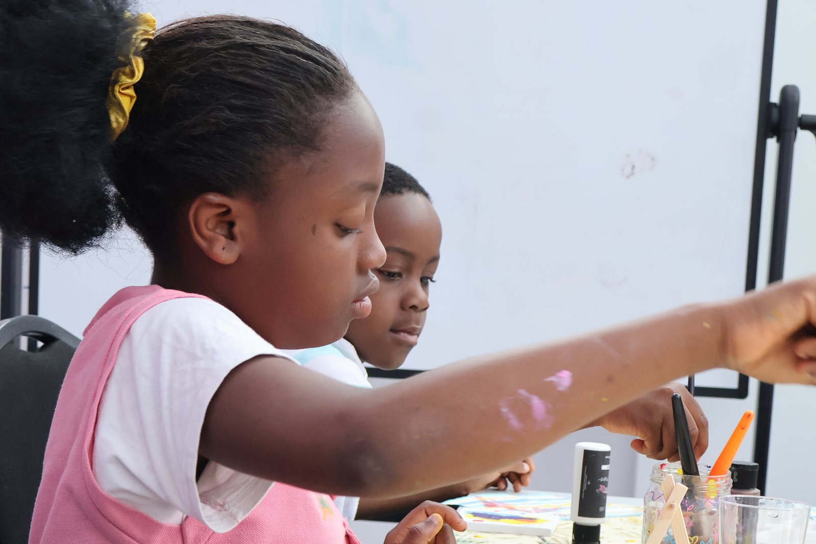 A girl painting at a board, another young person working alongside her.